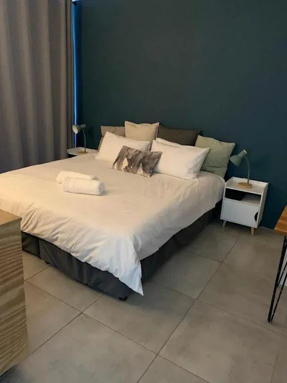 Modern bedroom with white bedding, teal accent wall, and minimalist nightstand