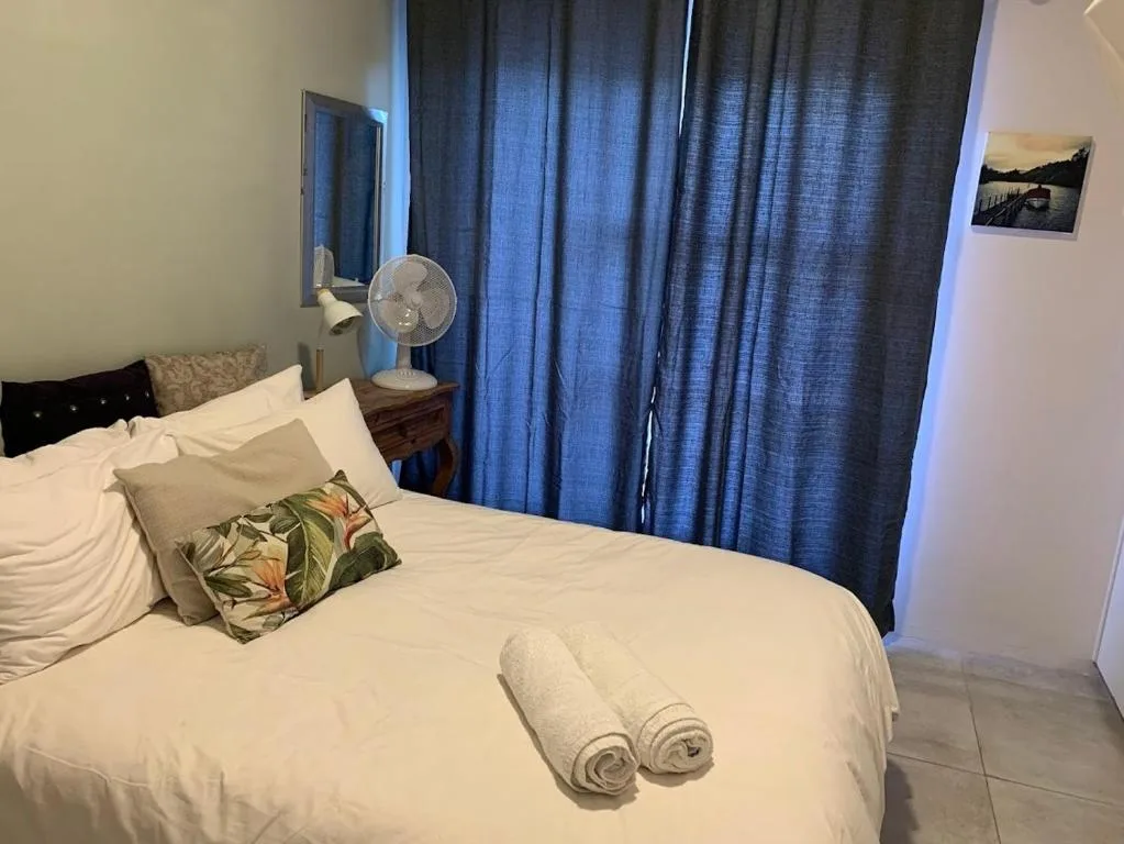 Neat bedroom with white bedding, tropical cushion, blue curtains, and fan