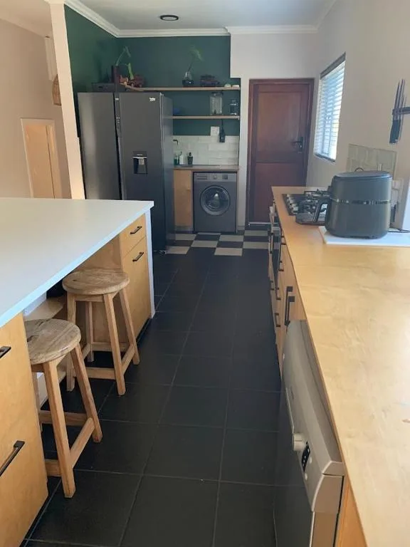 Modern kitchen with wooden cabinetry, stainless steel fridge, and black tiled flooring