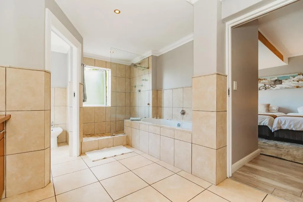 Spacious en-suite bathroom with walk-in shower, bathtub, and cream tile finishes
