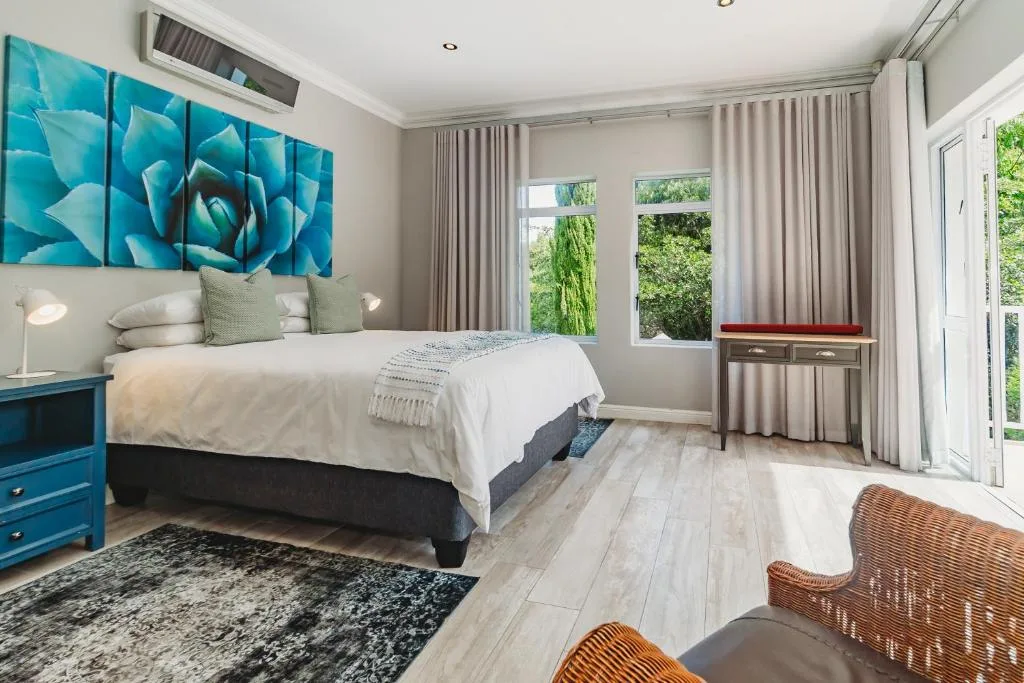 Bright modern bedroom with queen bed, turquoise artwork, and garden views