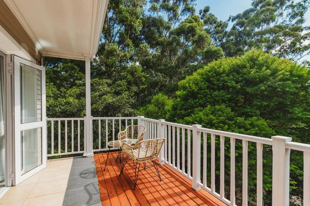 Wooden deck with white railing and wicker chairs overlooking lush gardens