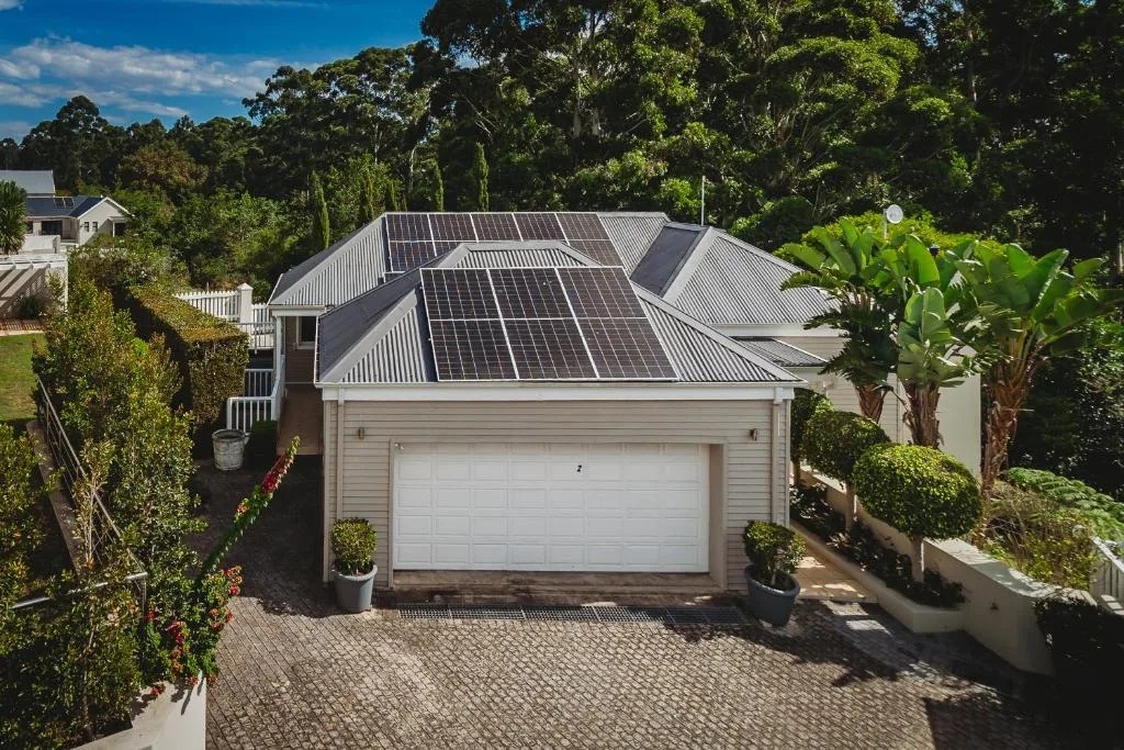 Modern home with solar panels on roof and paved driveway surrounded by gardens