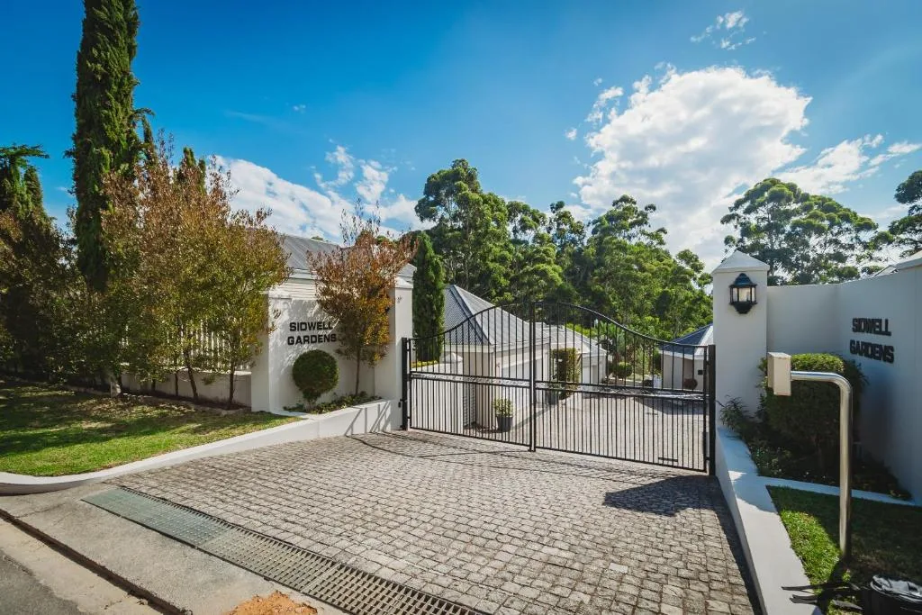 Modern white-walled property entrance with black metal gates and manicured gardens