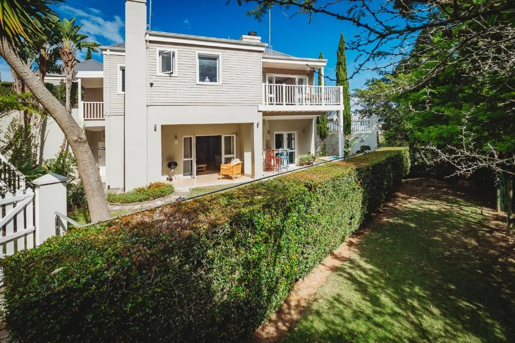 Modern white two-story house with manicured hedge garden and tree-lined pathway