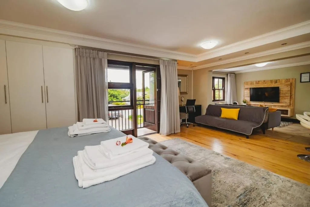 Spacious bedroom with double bed, lounge area, and deck access overlooking gardens