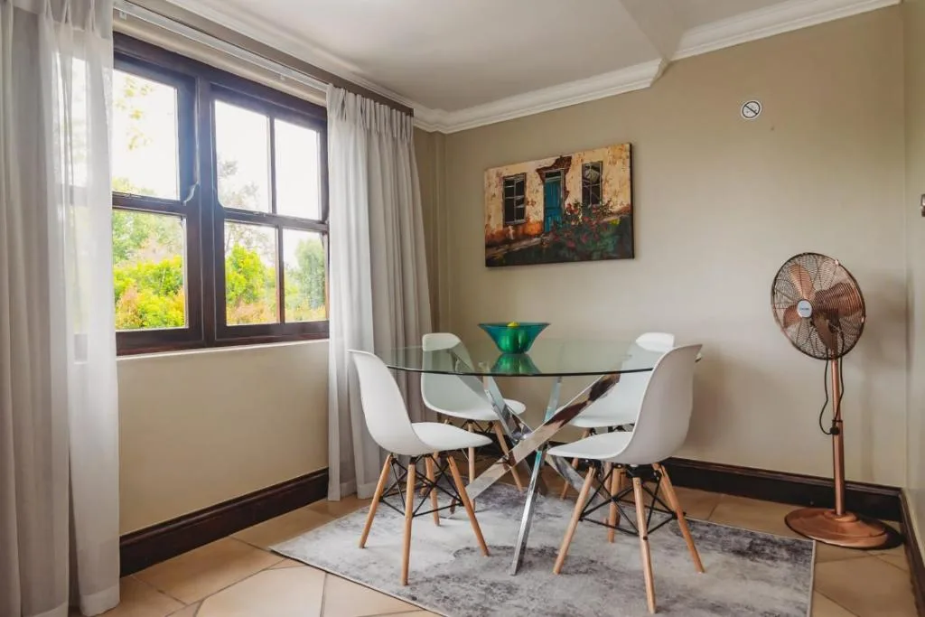 Bright dining area with glass table, white chairs, and garden views through windows