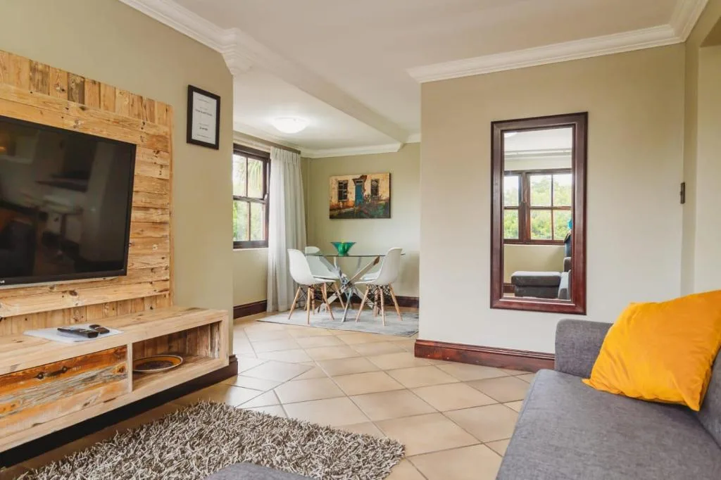 Open-plan lounge with gray sofa, wooden TV unit, and dining area beyond