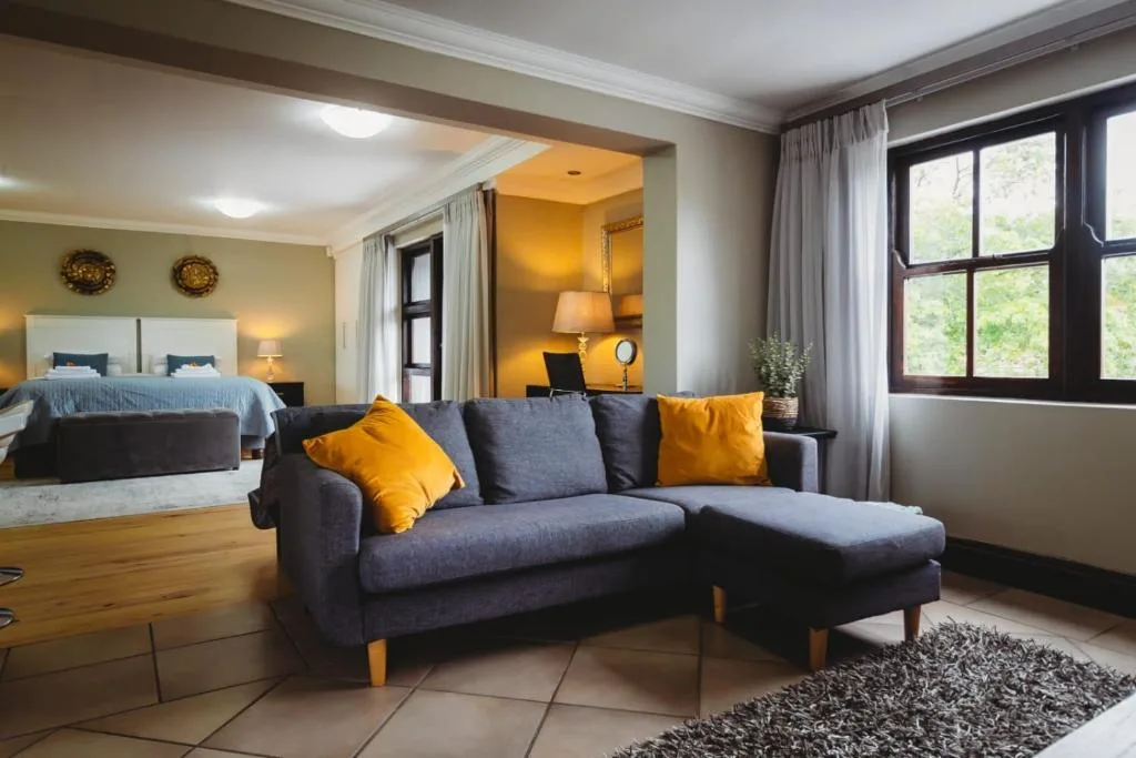 Open-plan lounge with blue sofa, yellow cushions, and bedroom visible beyond