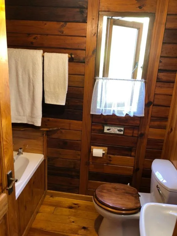 Wooden cabin bathroom with toilet, sink, bathtub and towel rails