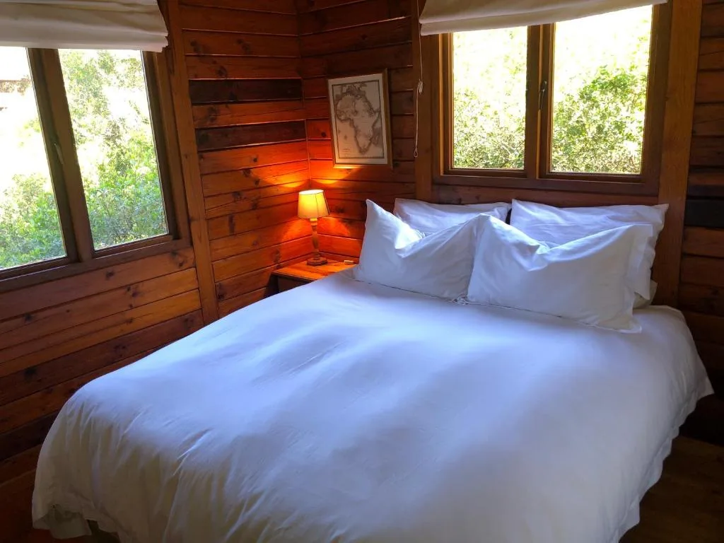 Wooden bedroom with white bedding, warm lighting, and forest views through windows
