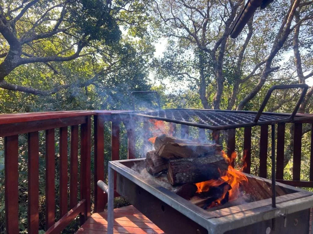 Active braai with flames under trees on wooden deck railing