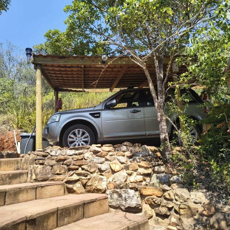 Silver SUV parked under wooden carport with stone walls and trees