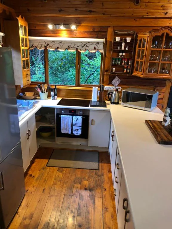 Bright kitchen with white cabinetry, wooden beams, and forest views through windows