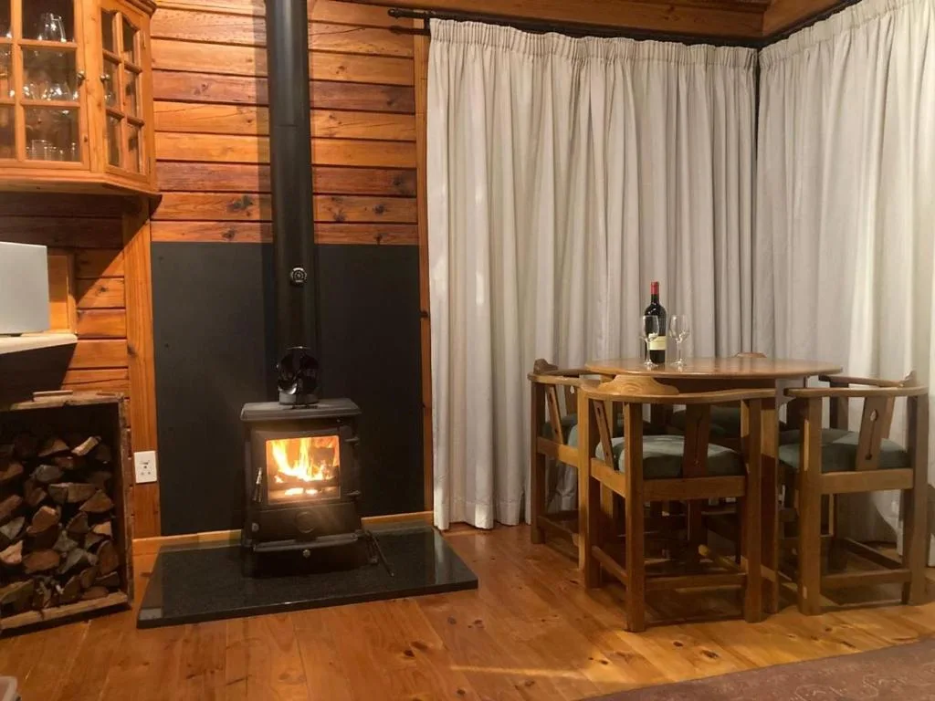 Cozy lounge with wood-burning stove, wooden dining table, and cream curtains