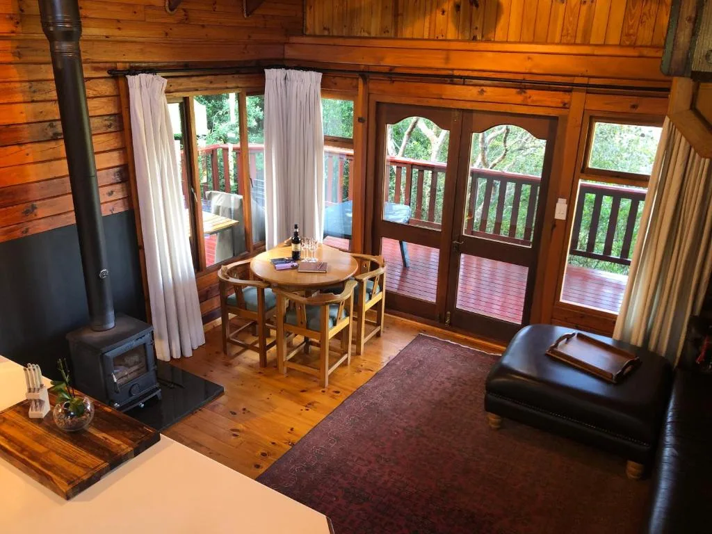 Open-plan lounge with wood stove, dining table, leather seating, and forest views