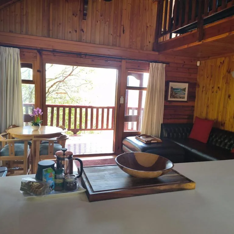 Wooden cabin lounge with black sofa, dining table, and deck view