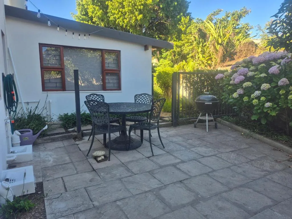 Patio seating area with dining table, chairs, and braai grill surrounded by flowering hydrangeas
