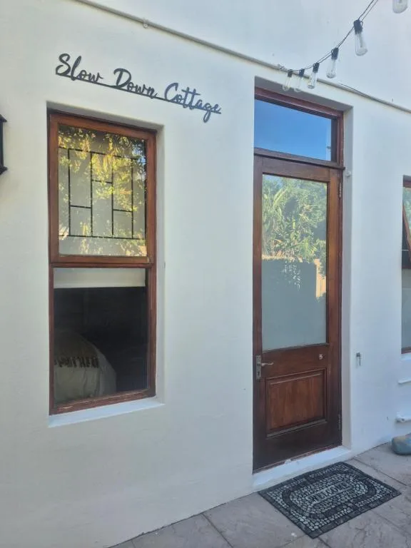 White cottage facade with wooden door and window, Slow Down Cottage sign