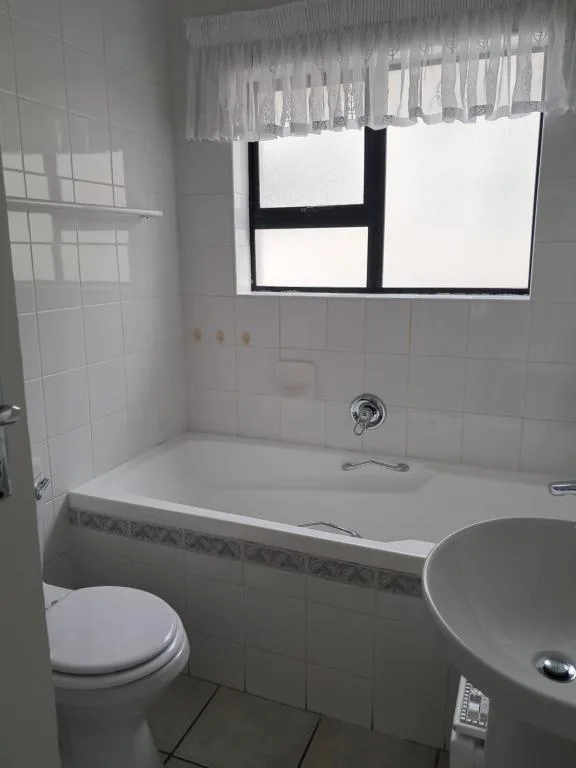 Clean bathroom with white tile walls, bathtub, toilet, and window
