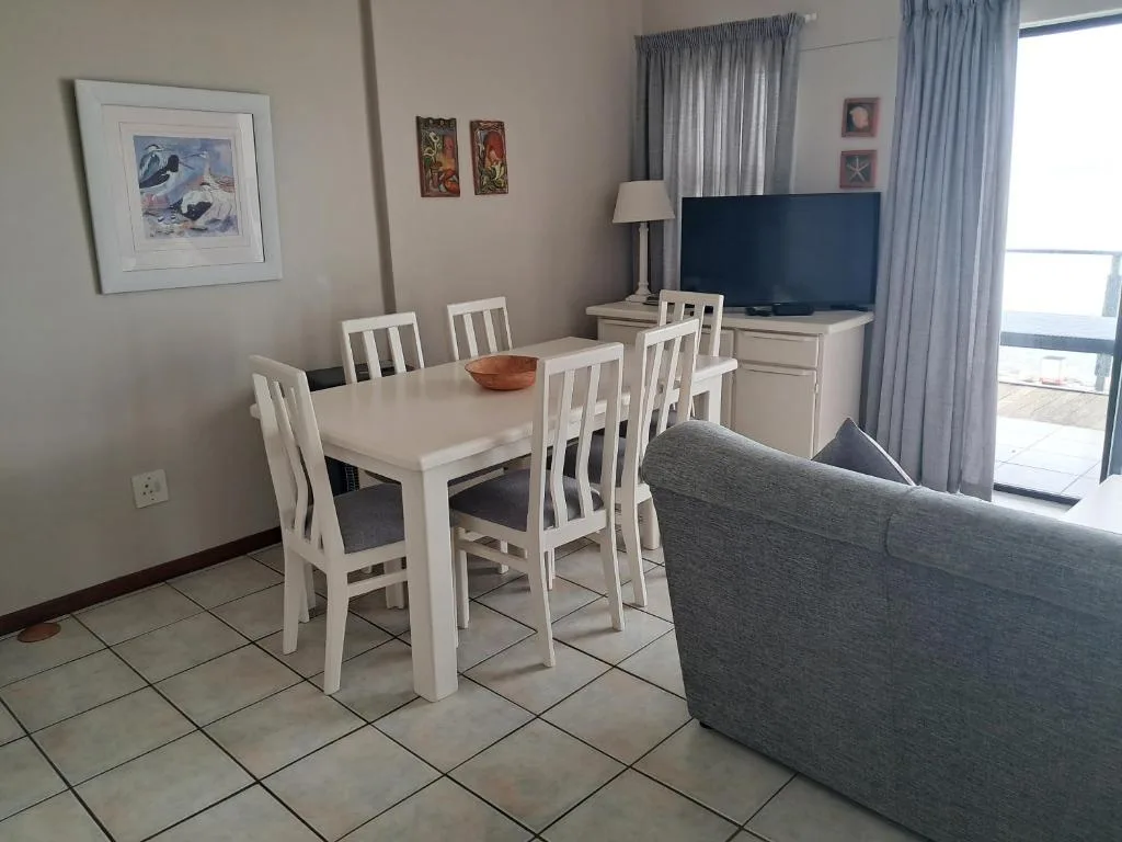Open-plan lounge and dining area with sofa, white dining table, and television