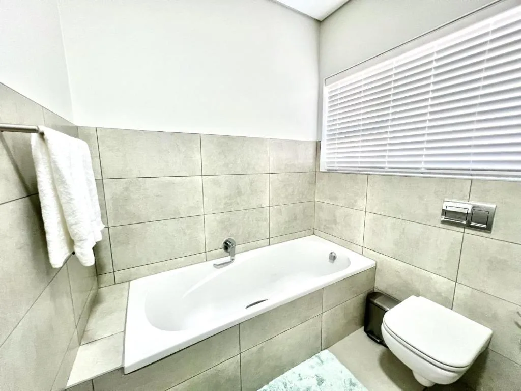 Modern bathroom with tiled walls, white bathtub, and wall-mounted toilet