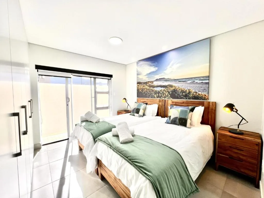 Bright bedroom with two beds, wooden furniture, and coastal landscape artwork