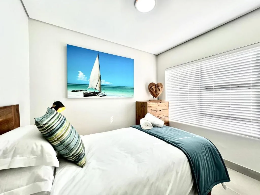 Bright bedroom with double bed, striped cushion, sailboat artwork, wooden nightstand
