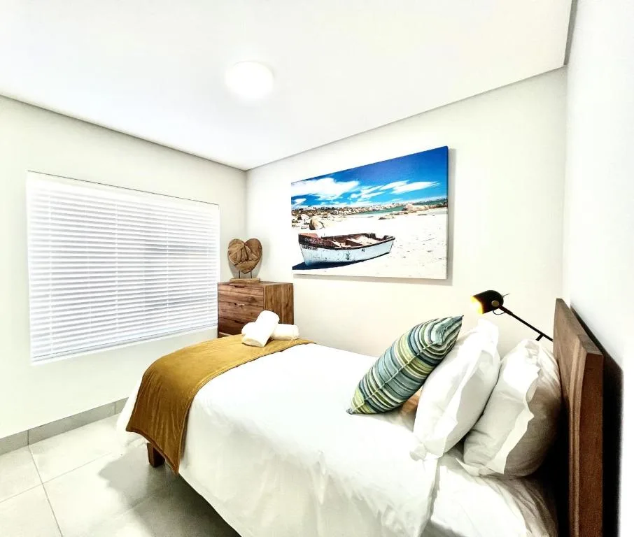 Bright bedroom with white bedding, wooden nightstand, and coastal artwork