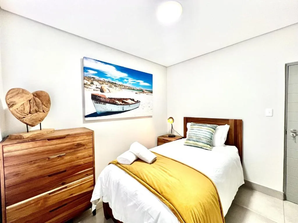 Modern bedroom with wooden bed frame, yellow throw, and coastal boat artwork