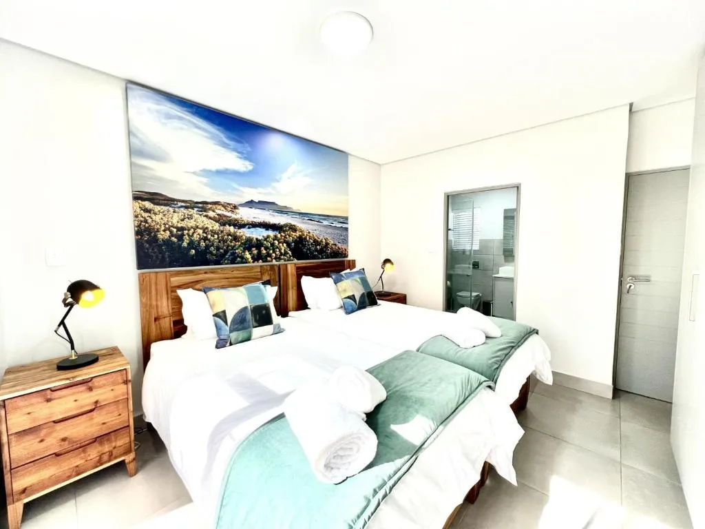 Bright bedroom with two beds, wooden nightstand, and scenic landscape artwork above headboard
