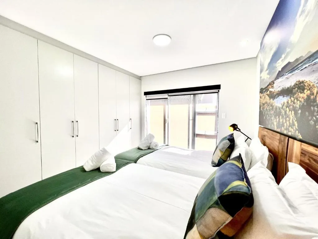 Bright bedroom with two beds, white cabinetry, and glass doors to outdoor space