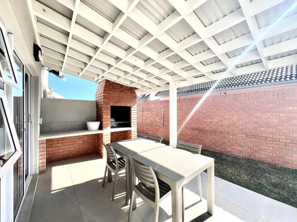 Covered outdoor patio with dining table, built-in braai, and brick walls