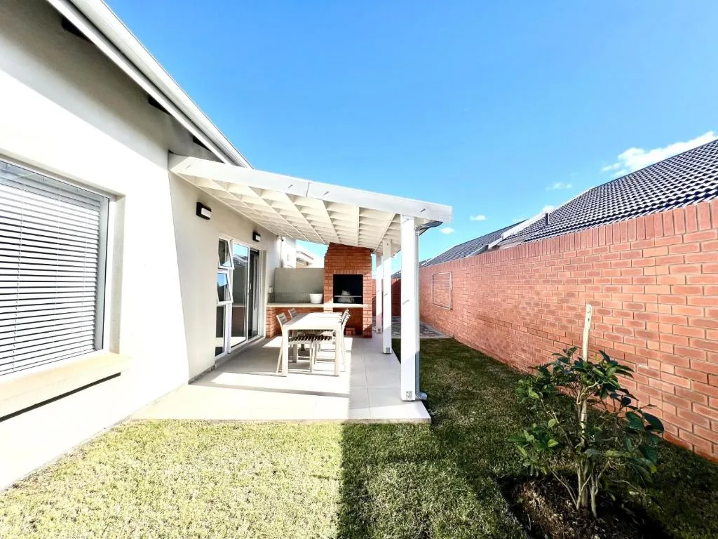 Covered patio with white pergola, seating area, and brick braai