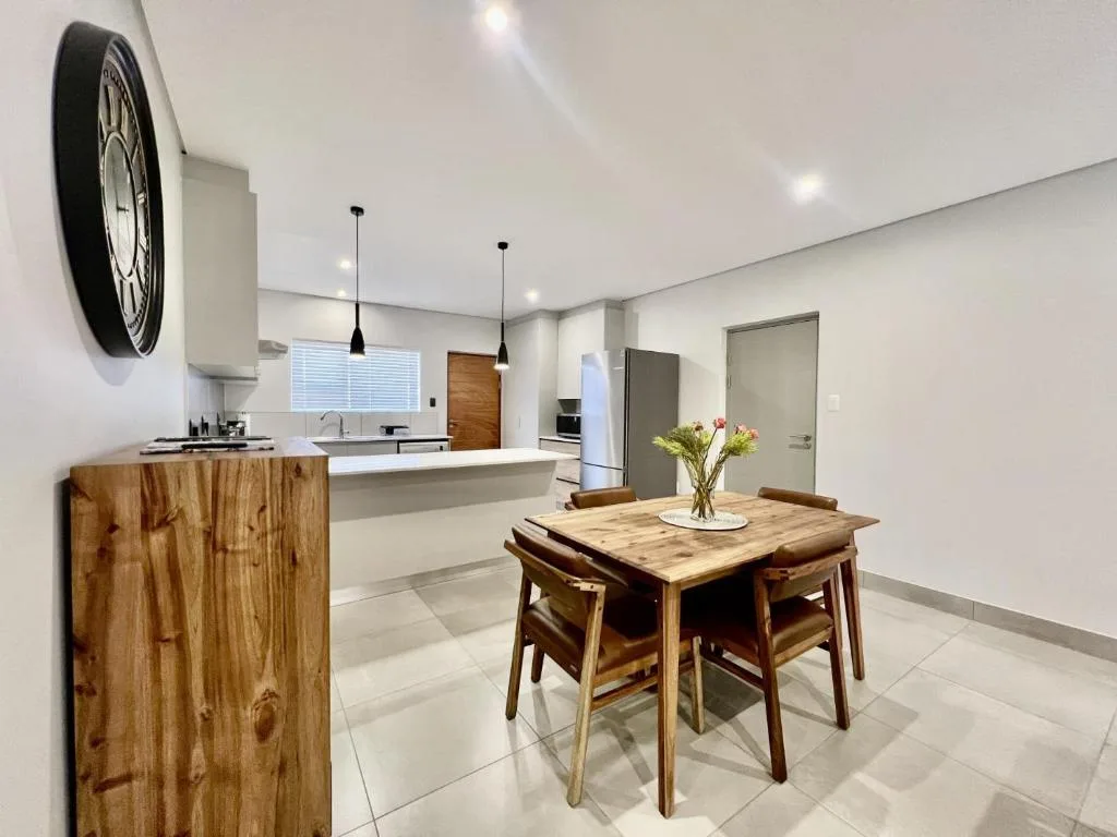 Modern dining table with wooden chairs, open kitchen visible beyond