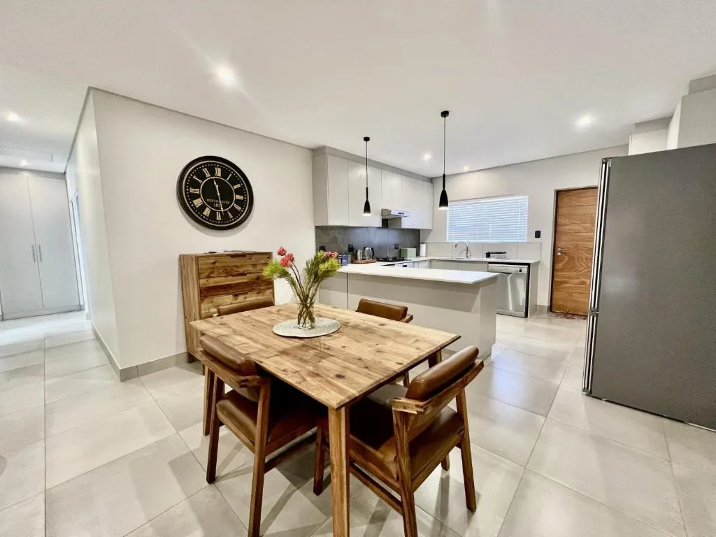 Modern dining area with wooden table, chairs, and open-plan kitchen beyond