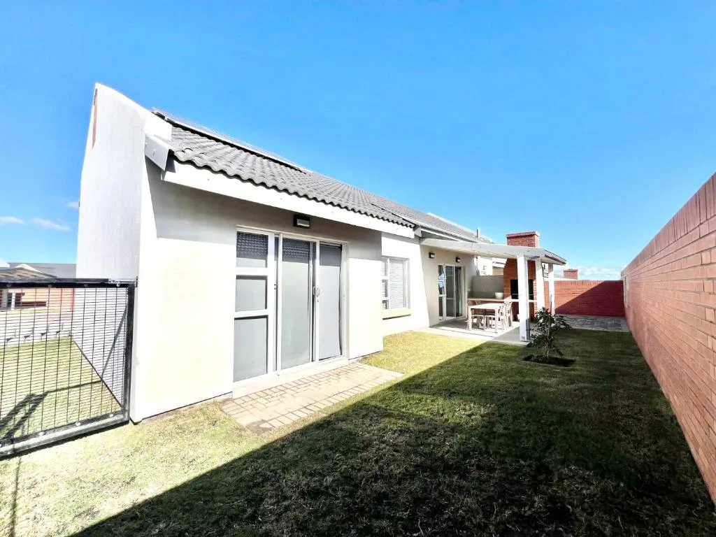 Modern white home with manicured lawn, patio area, and brick boundary walls