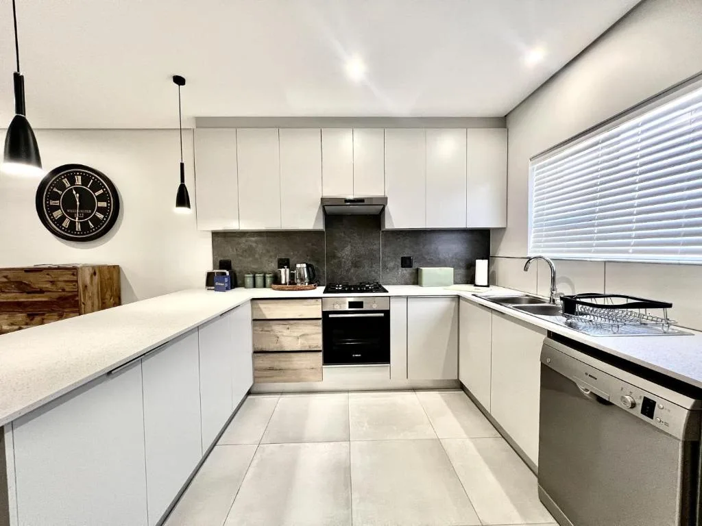 Modern white kitchen with black appliances, dark backsplash, and pendant lighting