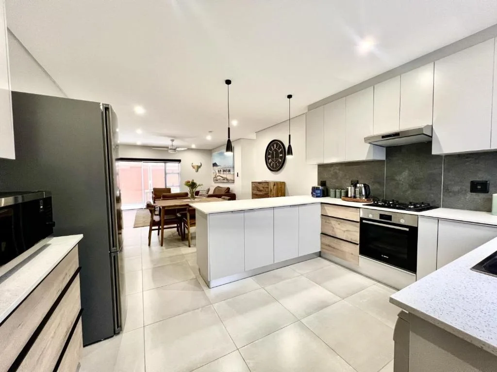 Modern open-plan kitchen with white cabinetry, dark backsplash, and stainless steel appliances