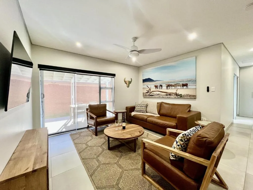 Modern lounge with brown leather sofa, armchairs, wooden coffee table, and sliding glass doors