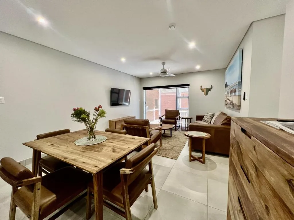 Open-plan living area with dining table, brown leather seating, and wall-mounted television