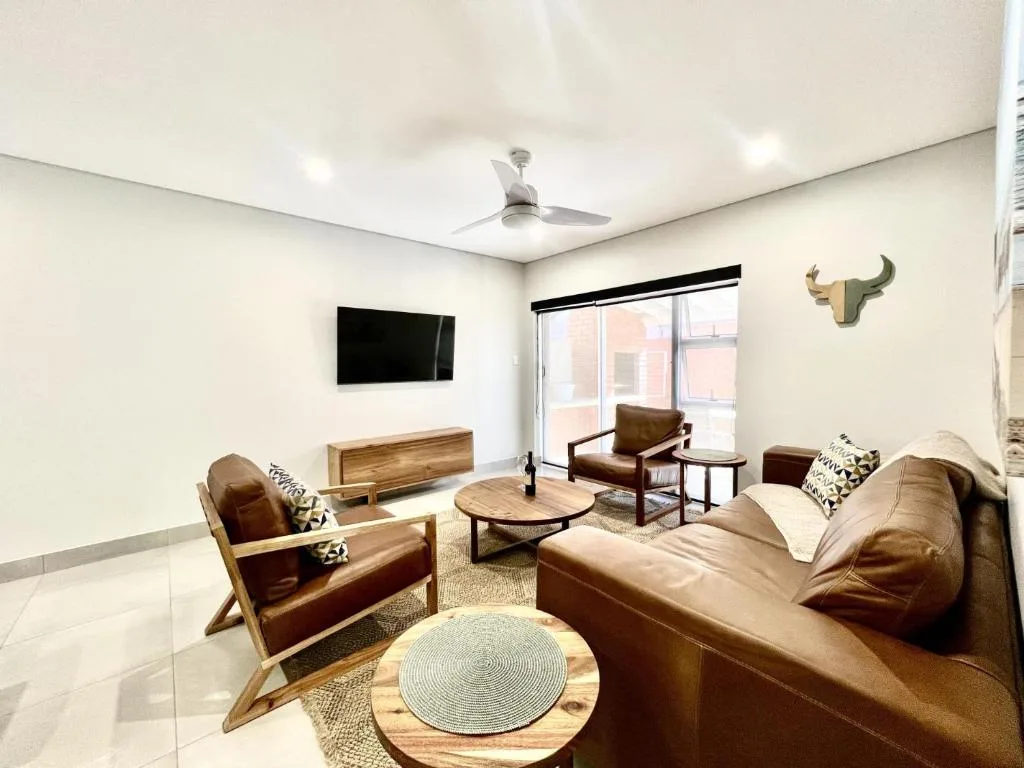 Modern lounge with brown leather seating, wall-mounted TV, and wooden accents