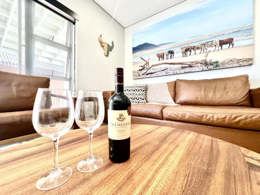 Leather sofa with wine bottle and glasses on wooden table, coastal artwork