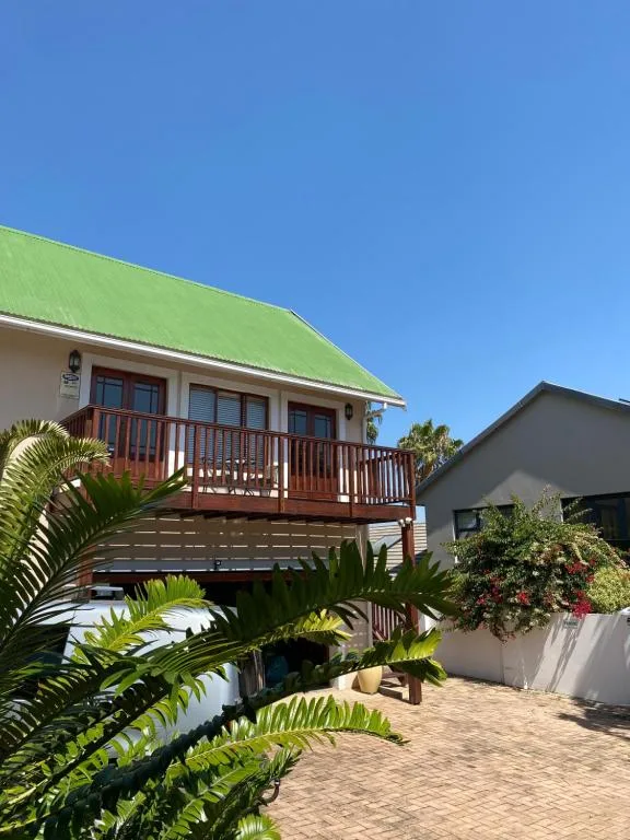 Modern self-catering home with bright green roof and wooden deck under clear blue sky