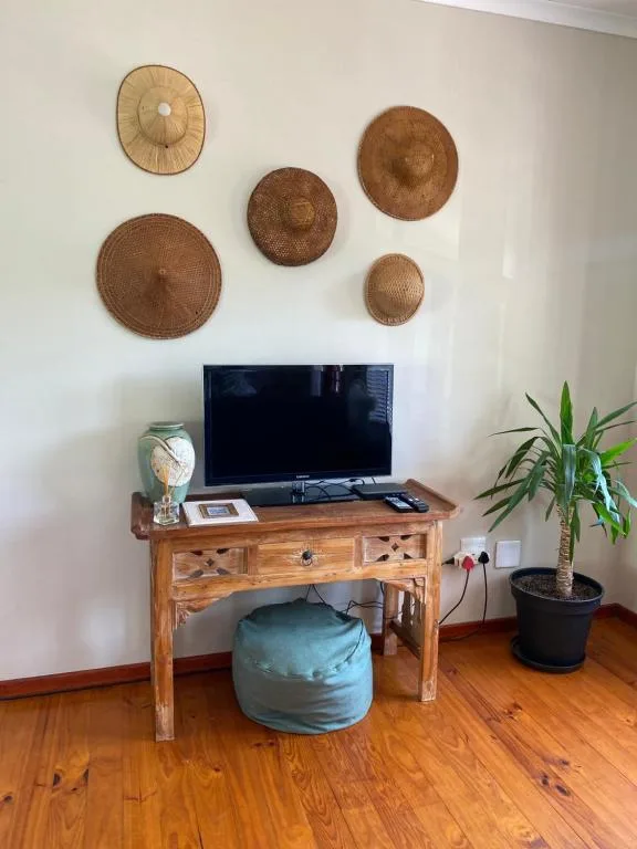 Living room with TV on wooden desk, woven basket wall art, potted plant