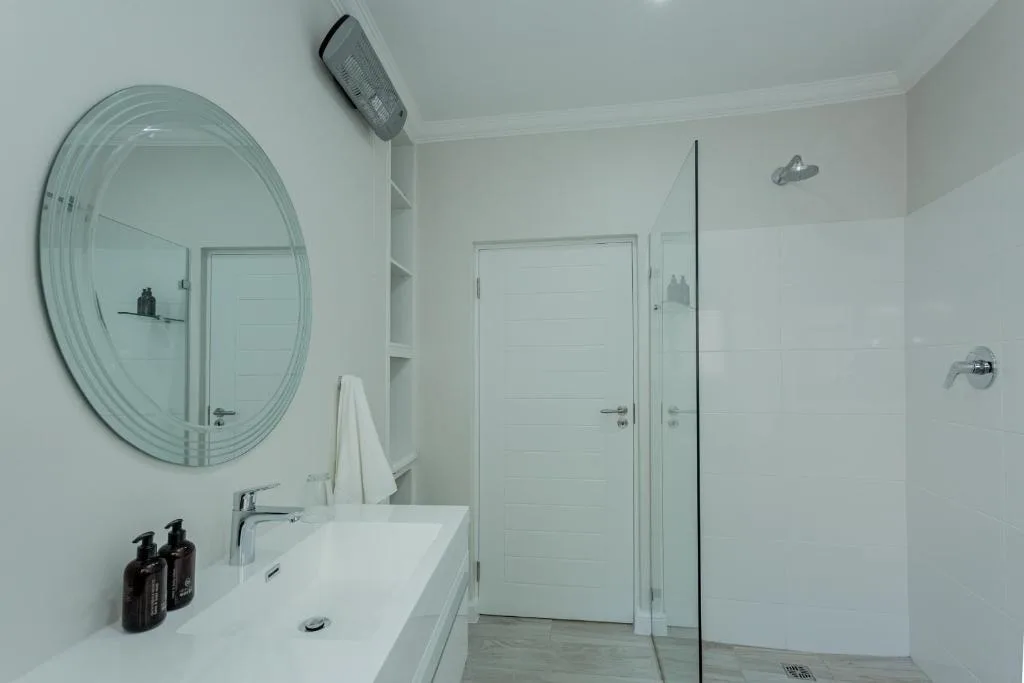 Modern bathroom with circular mirror, white vanity, and walk-in shower enclosure