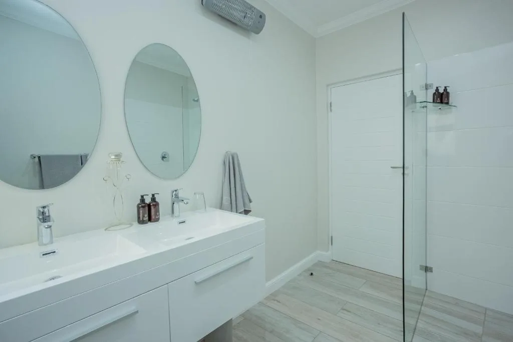 Modern bathroom with double vanity, circular mirrors, and glass shower enclosure