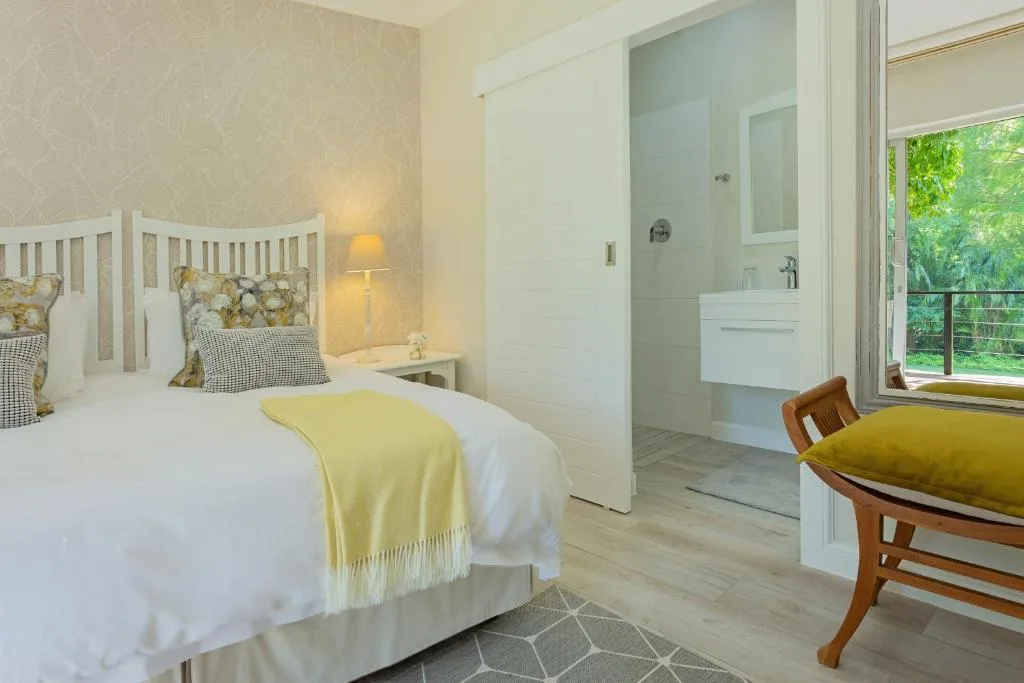Bright bedroom with white bed, yellow throw, ensuite bathroom visible through open door