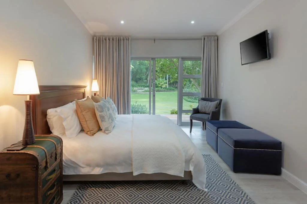 Spacious bedroom with queen bed, garden view doors, wall-mounted TV, and seating area