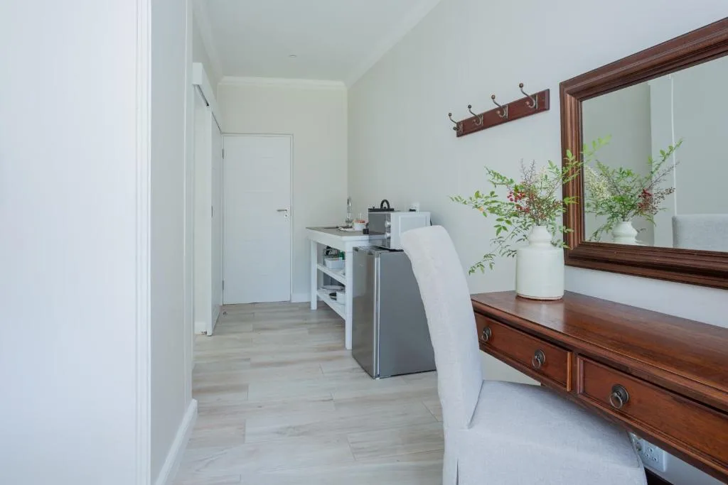 Modern bedroom with wooden dresser, mirror, potted plants, and kitchenette